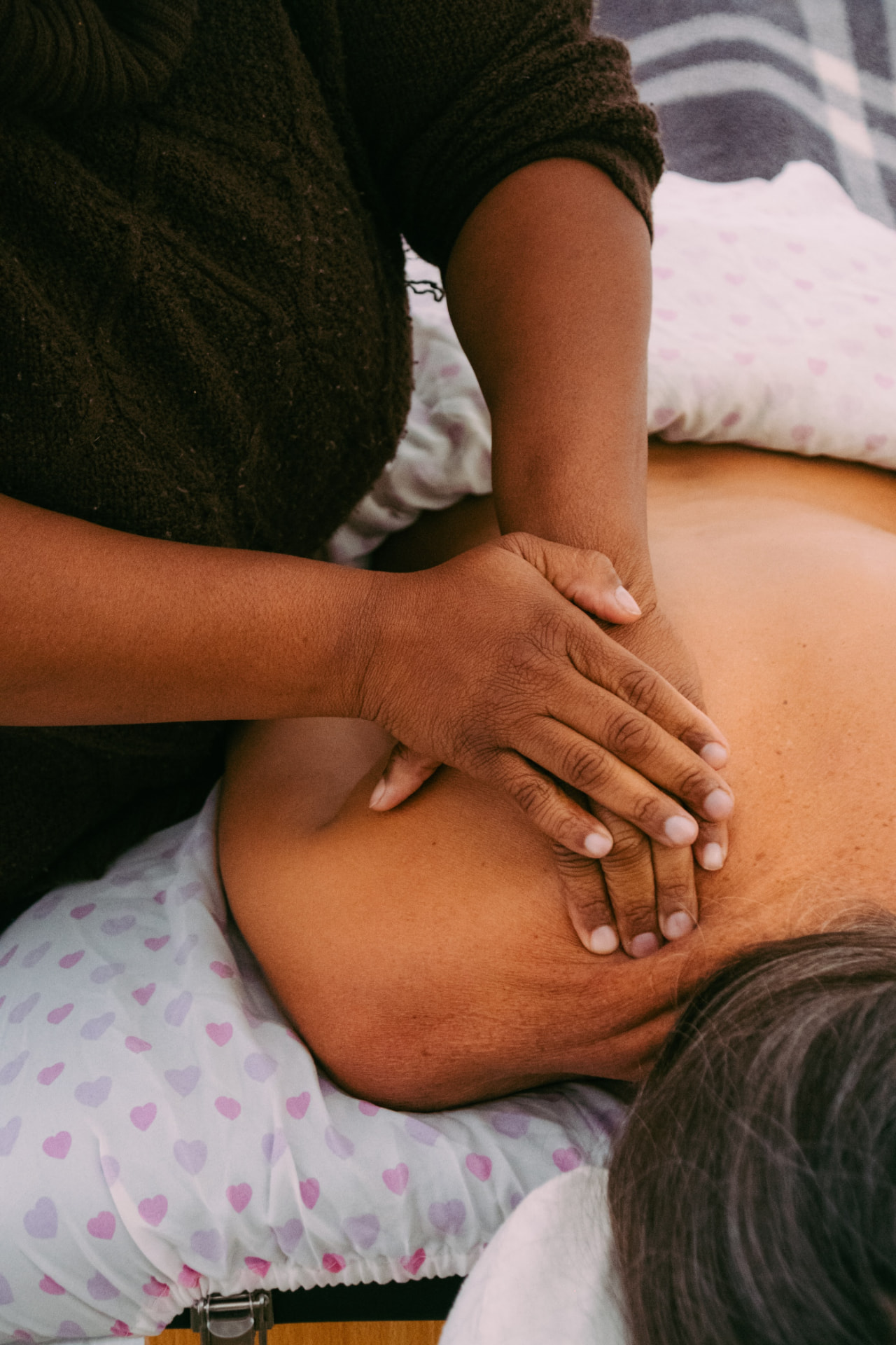 Dark-skinned hands giving grounded massage pressure to a client's upper back