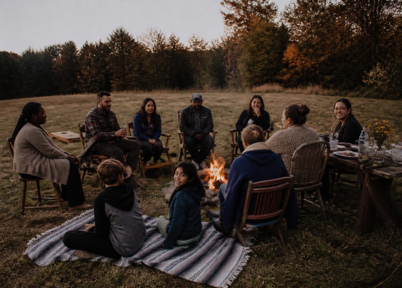 A diverse community gathered around a fire at dusk